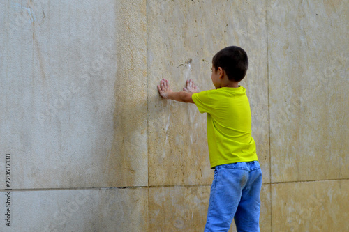 Мальчик приложил руки к бетонной стене по которой льется вода. в парке.