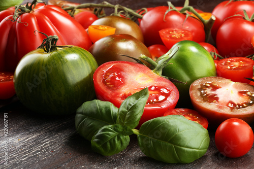 various colorful tomatoes and basil leaves on rustic table.