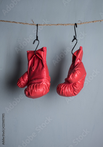 Red boxing mitts hanging on the gray wall.