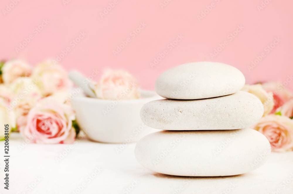 White spa stones on table set with roses and pink background, relaxing aromatherapy. 