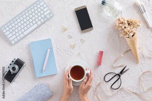 Flat lay of femamle desk workspace with flowers, computer keyboard, vintage scissors, diary, mobile phone on white concrete background, view from above