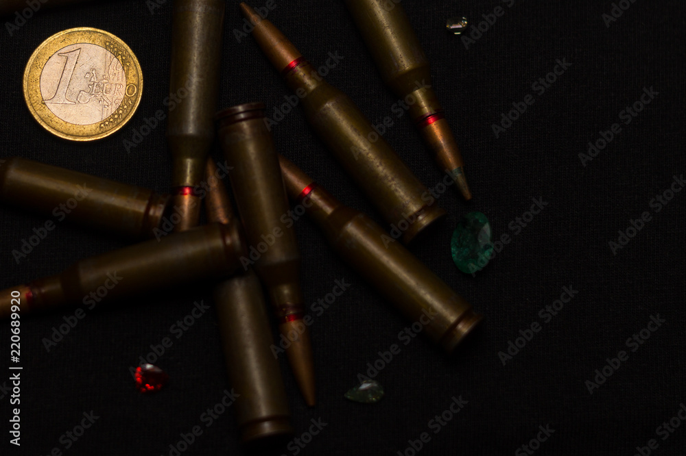 Rifle ammo around one euro coin wigh gemstones on black background. Symbolizes the war for money and one of the world's problems. Rifle ammo around one euro coin wigh gemstones on black background. Symbolizes the war for money and one of the world's problems.