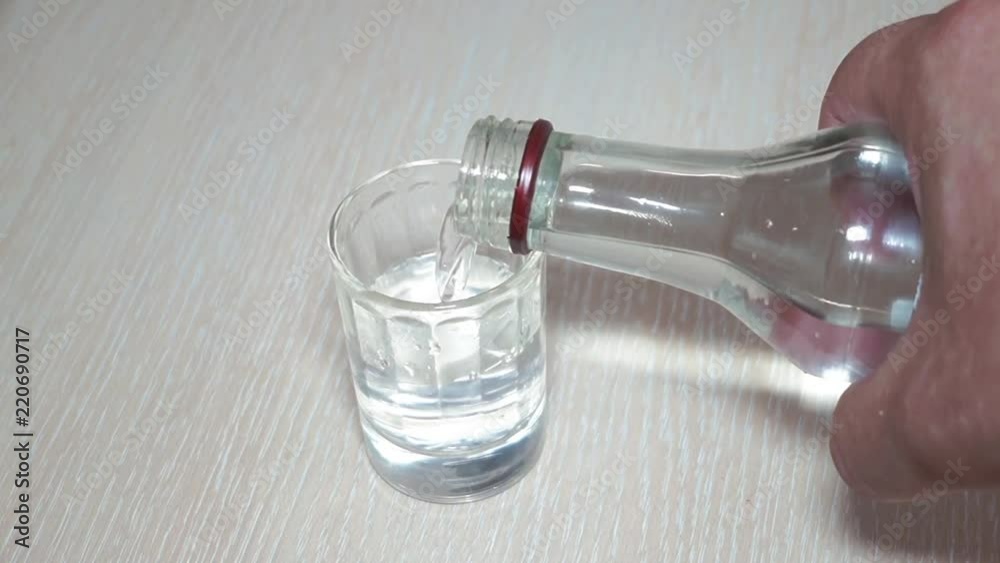 Pours the vodka. Against the background of the table. A large stack. Close-up. Pours the vodka. Against the background of the table. A large stack. Close-up.