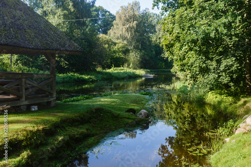 an old building, a canopy with a straw roof and a river that flows along both sides; Rural landscape with fallen river and river; rest near the river in fresh air