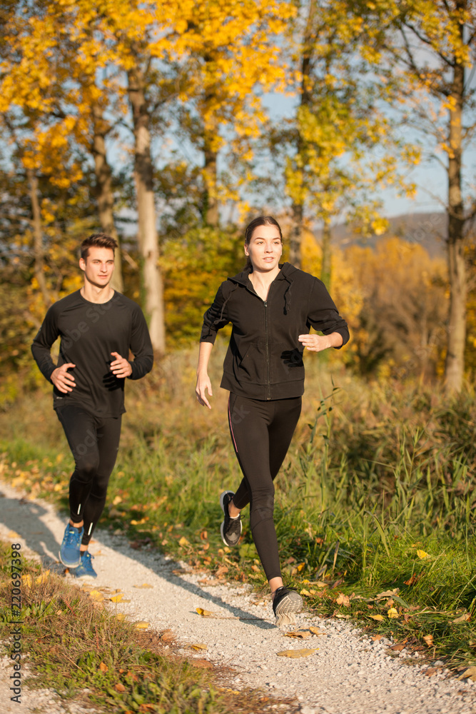 Obraz premium Young veautiful couple runs on a path in park on autumn afternoon