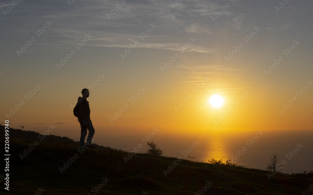 hiker in the backlight by mountain area with the sun in the background