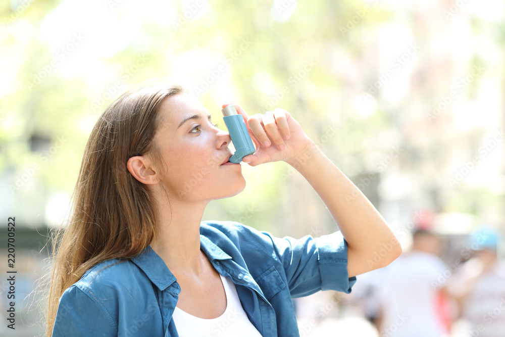 Asthmatic woman using a inhaler outdoors Asthmatic woman using a inhaler outdoors