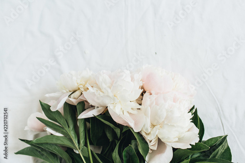 Fototapeta Naklejka Na Ścianę i Meble -  Flat lay, top view of white peonies flower bouquet on white blanket background. Minimal summer floral concept.