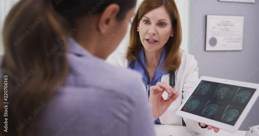 Young attracive latina patient reviewing ct scan of cranium with mid aged doctor Young attracive latina patient reviewing ct scan of cranium with mid aged doctor