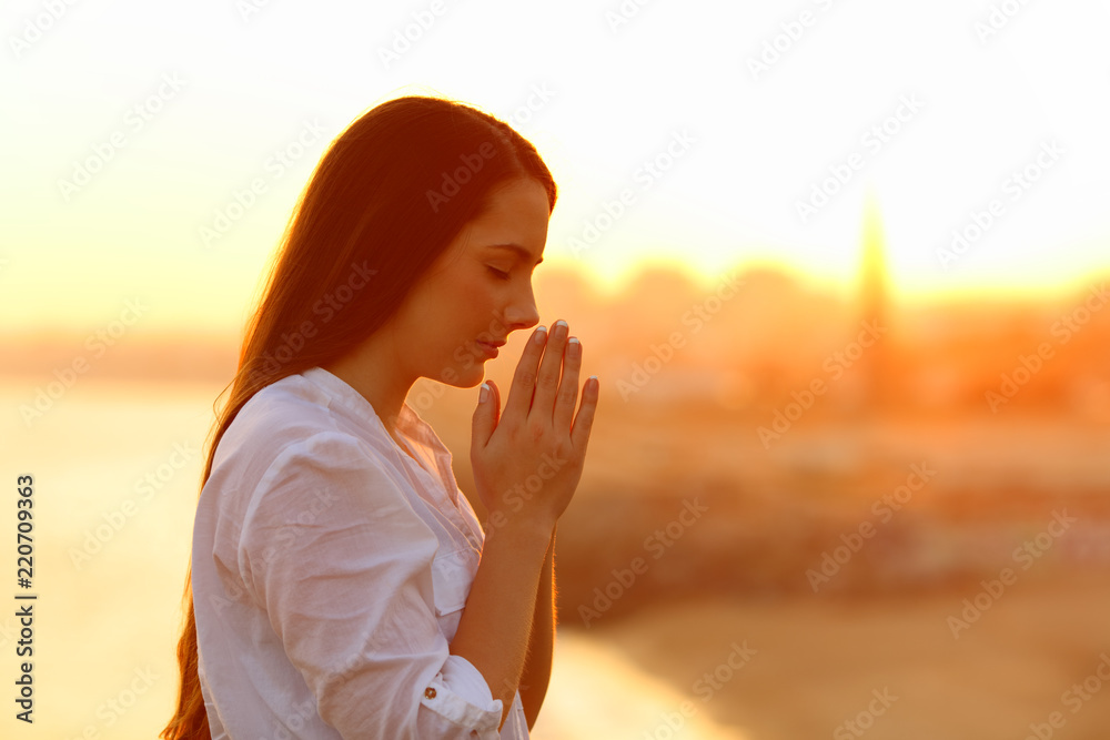 Fototapeta premium Profile of a concentrated woman praying at sunset