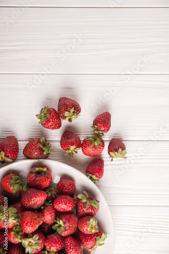 Fresh strawberries in a plate on a white wooden background.