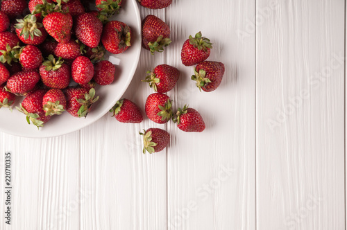 Fresh strawberries in a plate on a white wooden background.