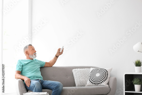 Senior man with air conditioner remote control at home photo