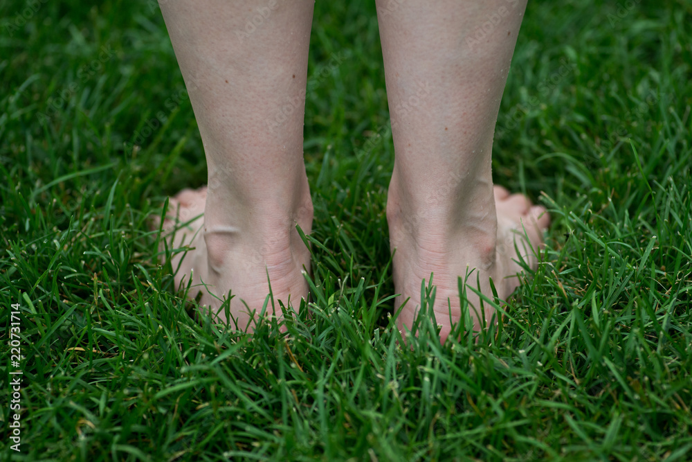 Woman standing on the grass with bare feet. Walking barefoot. Grounding.