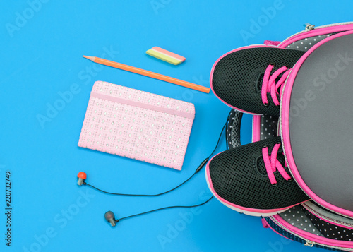 Kids sneakers in school backpack and school supplies on blue background. Flat lay.