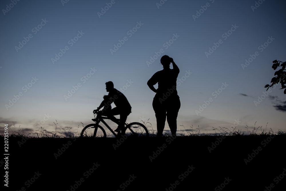 Silhouette of a woman, and man carrying baby on bike - outdoors Silhouette of a woman, and man carrying baby on bike - outdoors