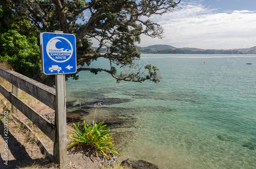 Coast in Mercury Bay, Coromandel, New Zealand, on a calm , sunny day with a tsunami evacuation route sign in the foreground.