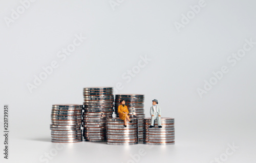 A miniature old man and a miniature old woman sitting on a pile of coins.