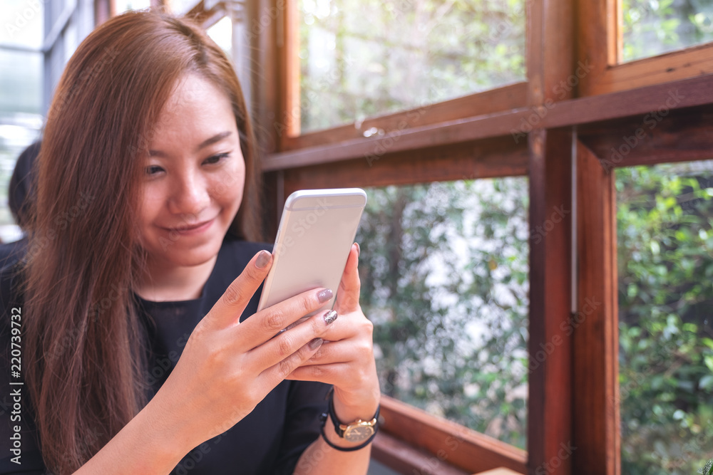 Closeup image of a beautiful Asian woman holding , using and looking at smart phone with feeling happy