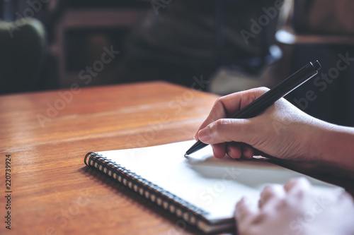 Canvas Print Closeup image of a hand writing down on a white blank notebook on wooden table
