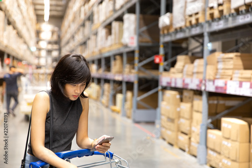 An asian woman doing shopping online via mobile phone in the warehouse.