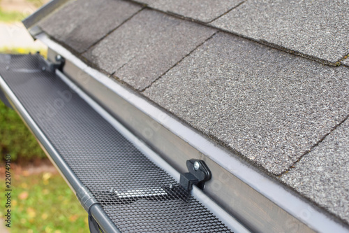 Plastic guard over new dark grey plastic rain gutter on asphalt shingles roof at shallow depth of field.