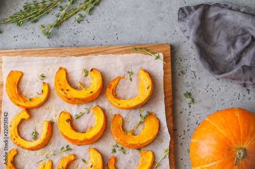Baked pumpkin slices with thyme on a wooden board over grey table. Seasonal food vegetarian recipe. Top view, flat lay.