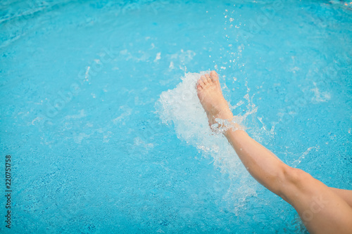 female legs splashing water in blue swimming pool, selective focus
