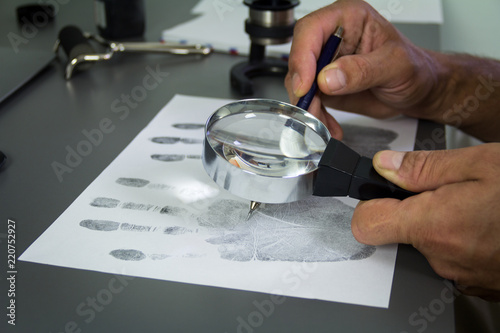 The investigation of the crime. The forensic expert studies the fingerprints taken of a suspect, with the help of a magnifier photo
