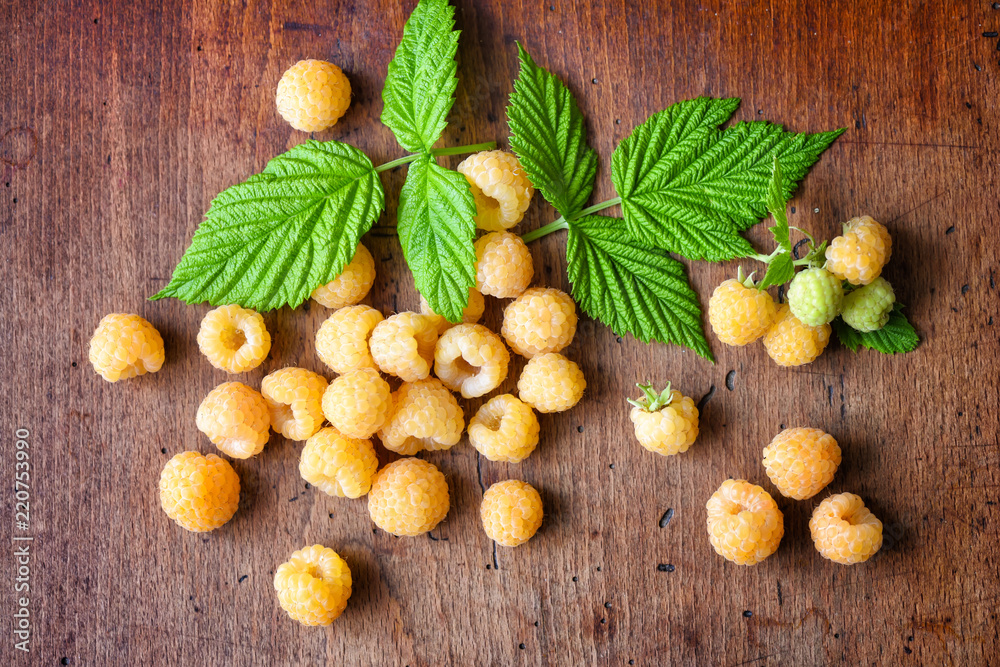 Ripe yellow raspberries with leaves on the old wooden background. Top view