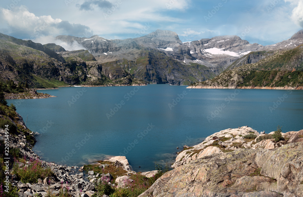 Panoramic View of a dammed lake high in the alpine peaks of Switzerland. Mountains and rocks surround the blue lake an all sides. Some snow still remains on the top Peaks