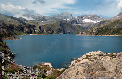Panoramic View of a dammed lake high in the alpine peaks of Switzerland. Mountains and rocks surround the blue lake an all sides. Some snow still remains on the top Peaks