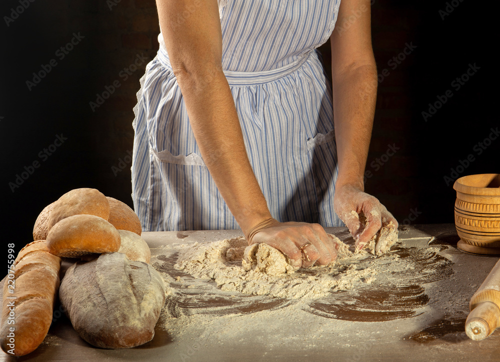 the girl in the apron kneads the dough for bread and buns on a black background