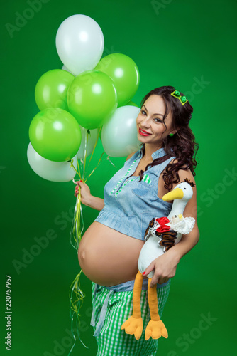 Pregnant woman with balloons and stork on a green background. He looks at his tummy, in anticipation