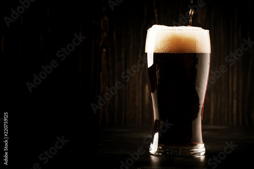 Dark english beer, ale or stout is poured into glass, dark bar counter, space for text, selective focus photo