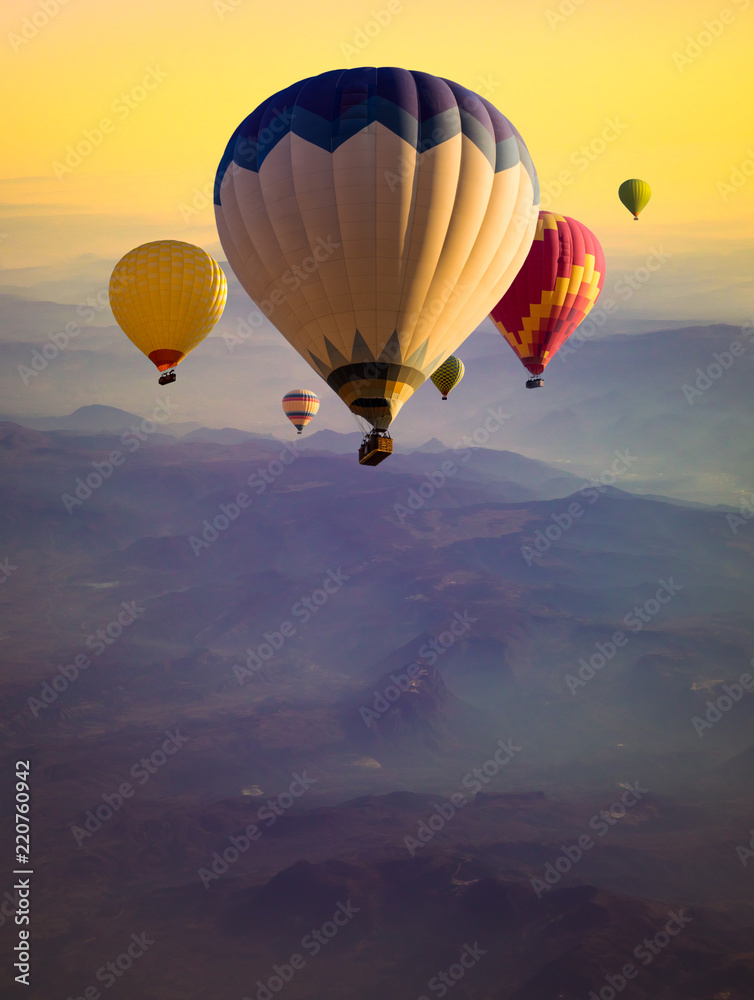 Fototapeta Multicolored hot air balloons flying over mountains hills at sunrise.