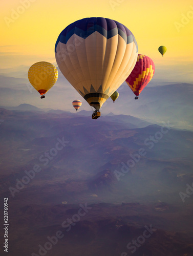 Multicolored hot air balloons flying over mountains hills at sunrise.