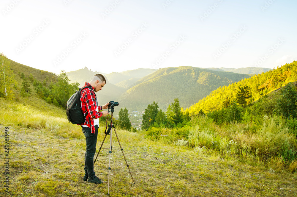 Young guy photographer takes pictures of nature with mountains on a SLR camera.