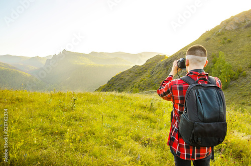 Young guy photographer takes pictures of nature with mountains on a SLR camera. photo