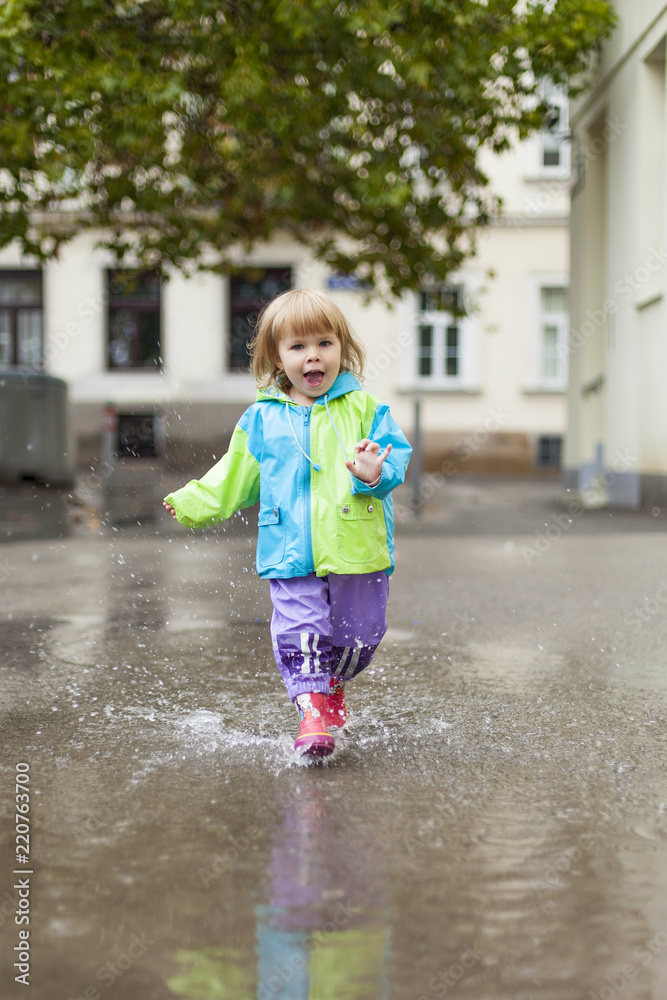 Naklejka premium Kleines Kind läuft in Regen durch Wasser Lacke. Little child girl running happy trough puddle.