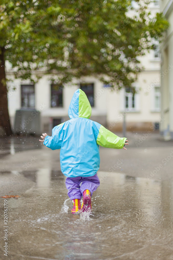 Kind in Regenmantel läuft durch Wasserlacke. Child in raincoat girl running  trough puddle. Stock Photo | Adobe Stock