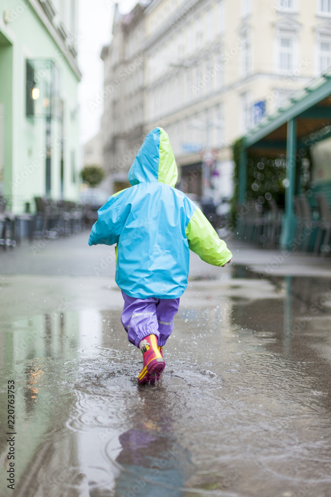 Child in raincoat girl running trough puddle water. Kind in Regenmantel  läuft durch Wasserpfütze. Stock Photo | Adobe Stock