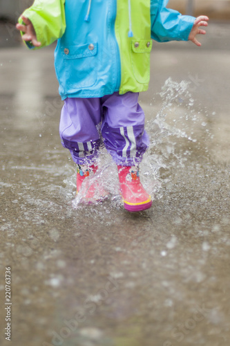 Kleines Kind läuft mit Gummistiefeln durch Wasser / Pfütze. Little child running trough puddle with rubber boots.