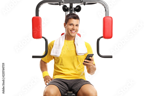 Young man sitting on an exercising machine and holding a mobile phone