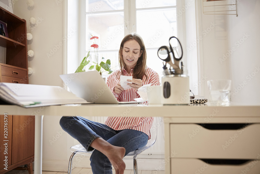 Full length of young woman examining financial bill while working from home Full length of young woman examining financial bill while working from home