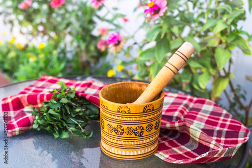 A wooden village mortar for herbs and spices with mint inside. Peppermint for cooking and cosmetology concept. Rural style with bright flowers