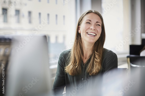 Smiling businesswoman looking away while sitting by window at office photo