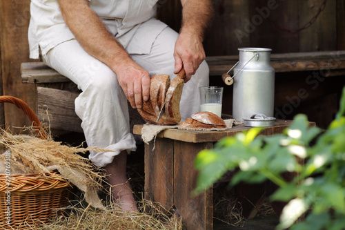 мужчина на скамейке в саду режет хлеб