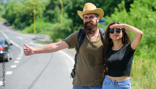 Couple hitchhikers travelling summer sunny day. Couple travelers man and girl hitchhiking at edge road nature background. Travellers try to stop car. Hitchhiking is one of cheapest ways of traveling