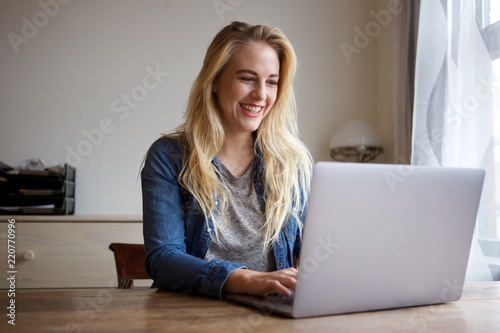 happy young blond woman using laptop at home